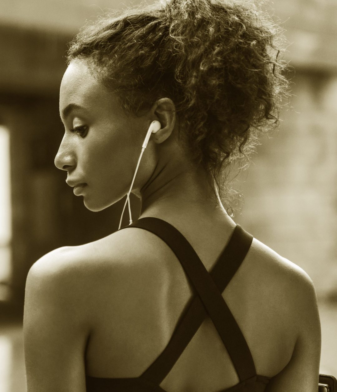 Rear view of female athlete with earphones standing outside in city and looking away Female Athlete
