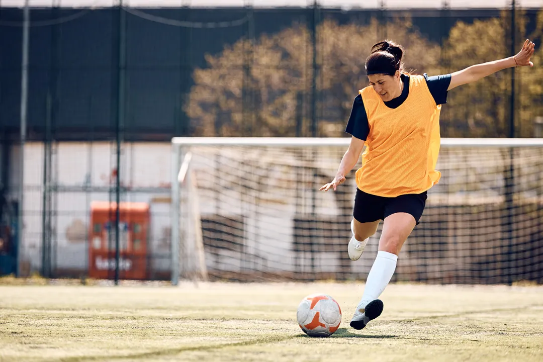 Female soccer player kicking the ball on playing field. Woman Kicking Soccer ball
